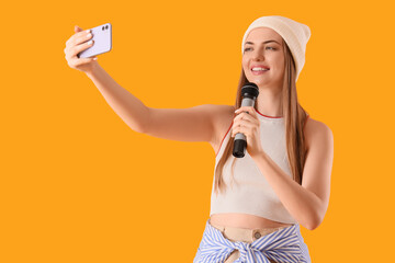 Young woman with mobile phone and microphone singing karaoke on yellow background