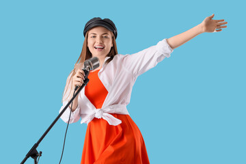 Young woman with microphone singing karaoke on blue background