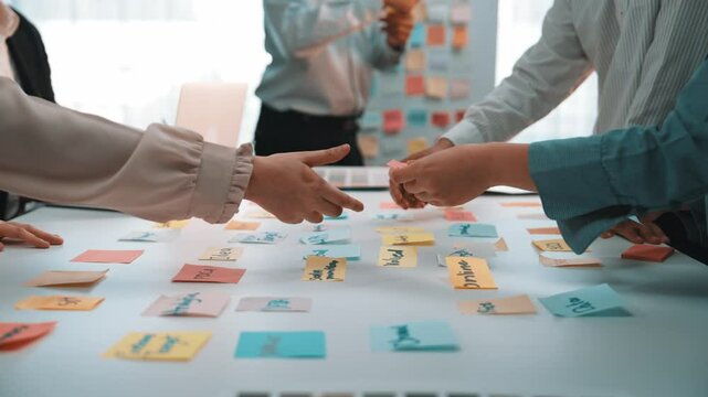 A dynamic creative meeting where team members engage in brainstorming ideas using colorful sticky notes, showcasing collaboration and innovative thinking in an office setting. SACTR