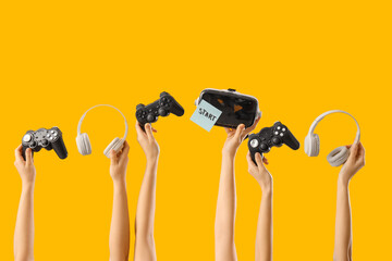 Female hands with game pads, VR glasses and headphones on yellow background © Pixel-Shot