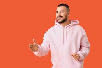 Young man reaching out for handshake on orange background. Rules concept
