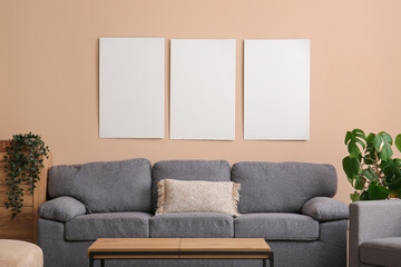Cozy sofa and blank posters on beige wall in room