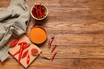 Bowl and spoon of red chili powder with peppers on wooden background