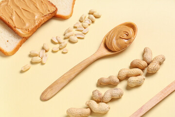 Wooden spoon with tasty peanut butter, toasts and nuts on beige background