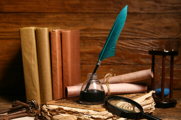 Old books with nib pen, inkwell, magnifying glass and scrolls on wooden background