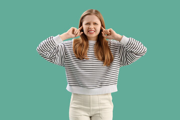 Young woman suffering from loud noise on green background