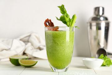 Glass of bloody Mary cocktail garnished with bacon and celery on white tile background