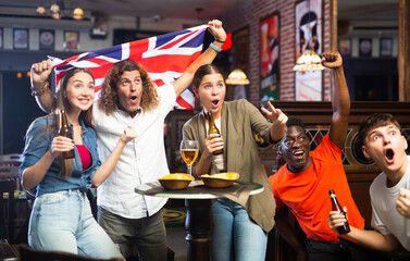 Obraz premium Group of emotional friends, football fans, having fun in sports bar, cheering for favorite British team together while watching match
