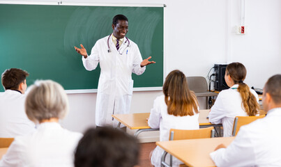 Positive african-american man doctor of medicine speaking to group of students in classroom in...