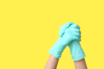 Female hands in medical gloves showing gratitude gesture on yellow background