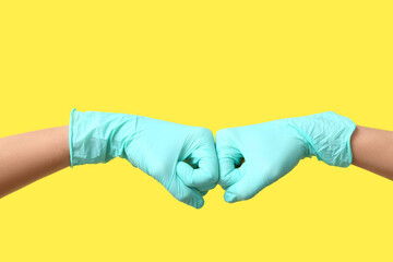 Female doctors in medical gloves giving fist bumps to each other on yellow background