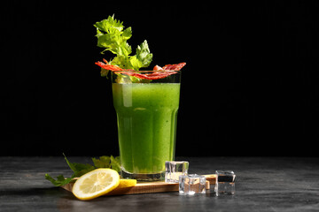 Glass of green bloody mary cocktail with bacon, celery and lemon on black background
