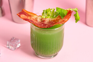 Glass of green bloody mary cocktail with bacon and celery on pink background, closeup