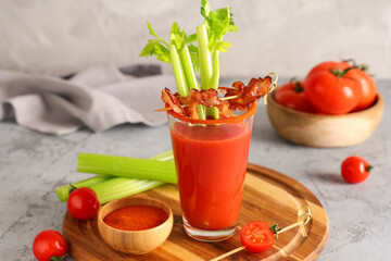 Glass of bloody mary cocktail with bacon, celery and bowl of spices on grey background