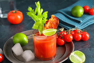 Glass of bloody mary cocktail with bacon, celery and lime on blue background, closeup