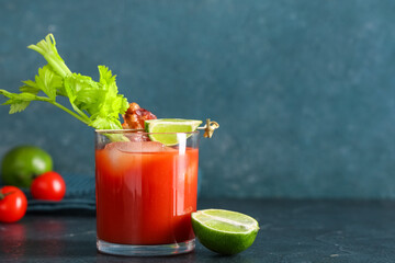 Glass of bloody mary cocktail with bacon, celery and lime on blue background