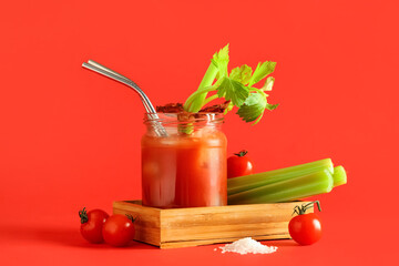 Mason jar of bloody mary cocktail with bacon and celery on red background