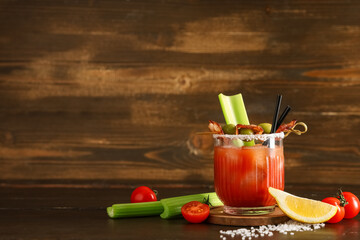 Glass of bloody mary cocktail with bacon, olives and celery on wooden background