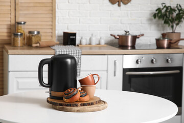 Electric kettle with tasty poppy buns and cups on table in kitchen