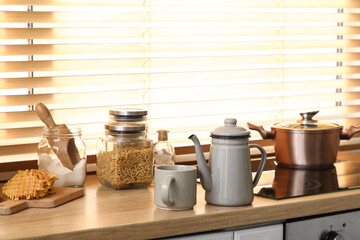 Teapot with tasty waffles and cup near stove on table in kitchen