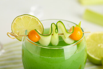 Glass of green bloody mary cocktail garnished with physalis berries, lime and cucumber slice on...