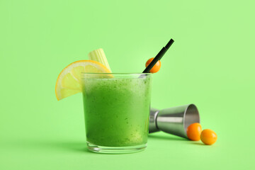 Glass of green bloody mary cocktail garnished with lemon and physalis berry on color background