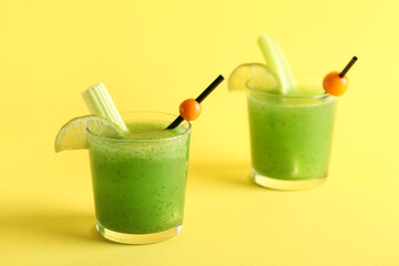Glasses of green bloody mary cocktail garnished with physalis berries and lime on yellow background