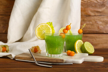 Glasses of green bloody mary cocktail garnished with physalis berries and lemon on wooden background