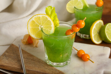 Glass of green bloody mary cocktail garnished with physalis berries and lemon on wooden background,...