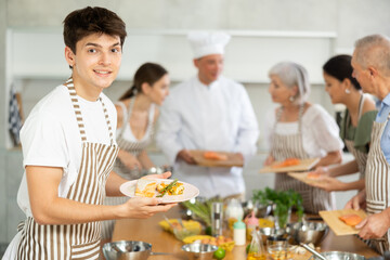 Happy smiling young culinary enthusiast participating in group cooking class, standing in striped...