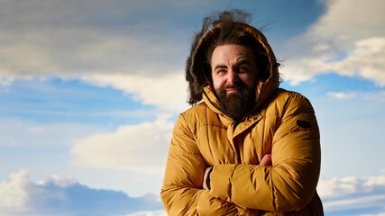 Adventure seeker climbing the mountain with extreme windy weather, feeling happy with his achievement. Young hiker feeling the cold wind on the hill top, scenic background. Camera B.