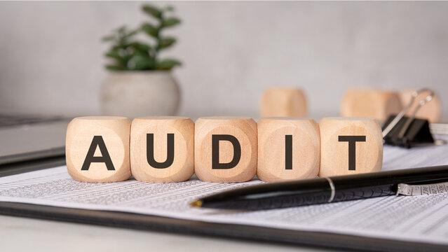 Audit concept with wooden blocks on financial documents, pen, and office supplies.