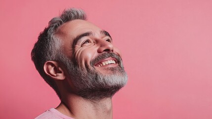 Obraz premium Portrait of a happy mature man with grey hair and beard looking up on a pink background studio shot