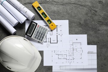 Different architectural drawings, hard hat, building level and calculator on grey table, flat lay
