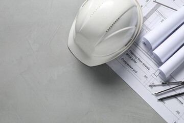 Different architectural drawings, hard hat, pencil and divider on grey table, flat lay. Space for...