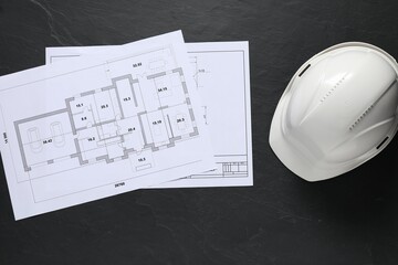 Different engineering drawings and hard hat on black table, flat lay. Space for text