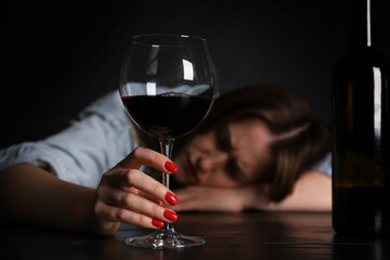 Alcohol addiction. Miserable woman with wine at table in dark, selective focus