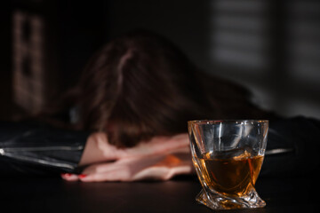 Alcohol addiction. Woman at table indoors, focus on glass of whiskey
