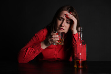 Alcohol addiction. Miserable woman drinking whiskey at table in dark