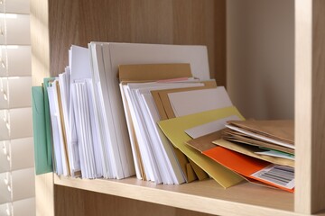 Different paper envelopes on wooden shelf in post office, closeup
