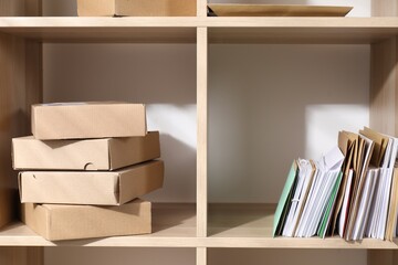 Different paper envelopes and parcels on wooden shelves in post office