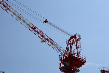 A large construction crane with a long, angled arm extending into the sky. Cables, pulleys, and a platform with ladders are visible, indicating an industrial or construct