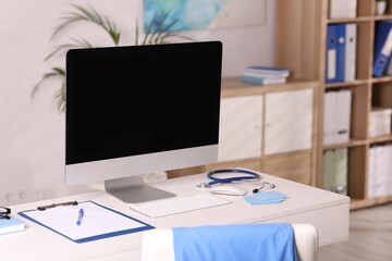 Doctor's workplace. Computer monitor, keyboard, mouse, stethoscope and stationery on white table in medical office