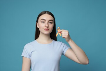 Multiple Sclerosis awareness. Young woman holding orange ribbon on light blue background