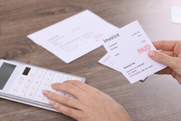 Obraz premium Paying bills. Woman with different invoices and calculator at wooden table indoors, closeup