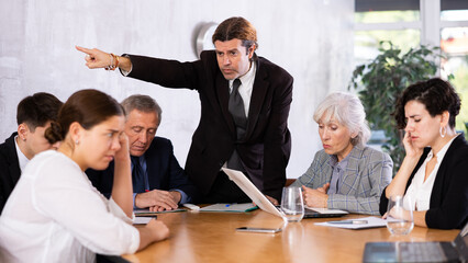 Irritated boss scolding subordinates, pointing out shortcomings and omissions in work during office meeting