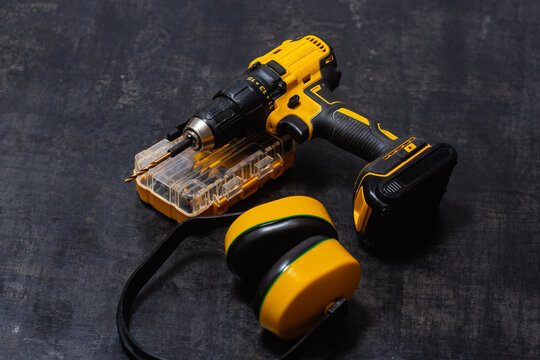 Yellow cordless drill drill with ear protection and bits on dark surface. Powerful tool for construction and DIY projects.