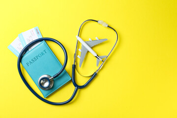 Medical tourism. Passport with tickets, stethoscope and airplane model on yellow background, top...