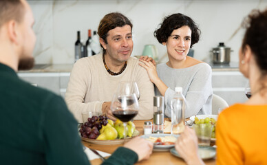 Group of happy celebrating holiday drinking and chatting at table at home