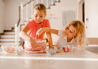 Two girls happily decorating homemade birthday cake with sprinkles in a sunny home kitchen